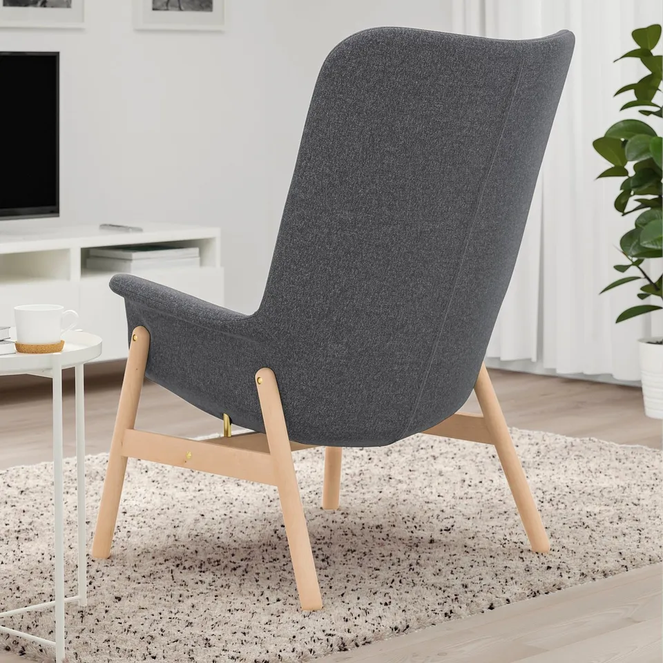 Dark grey high-back armchair with wooden legs on a speckled rug in living room.