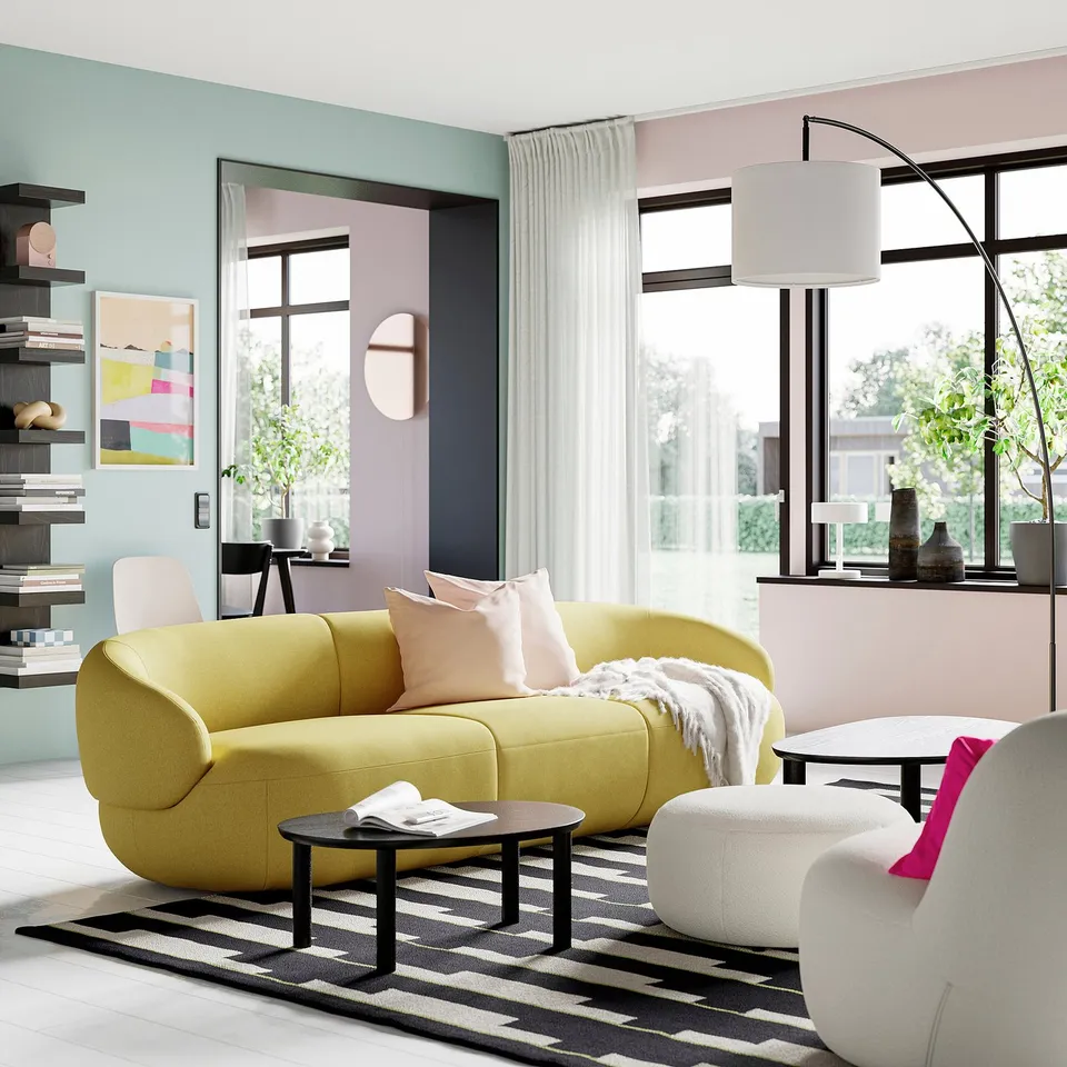 Modern living room with yellow sofa, black side table, black and white rug, and large windows. Table is small compared to other items.