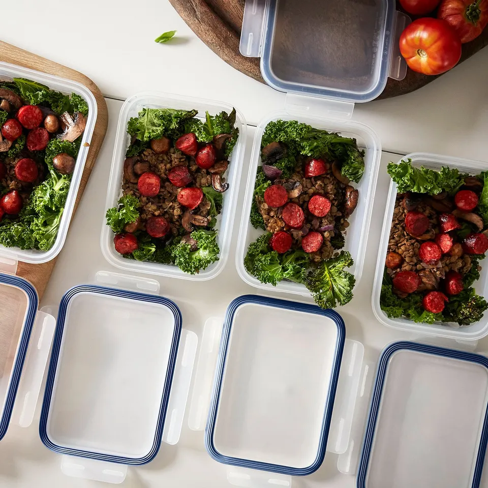 Meal prep containers with broccoli, sausage, lentils, and mushrooms, plus tomatoes and empty containers.