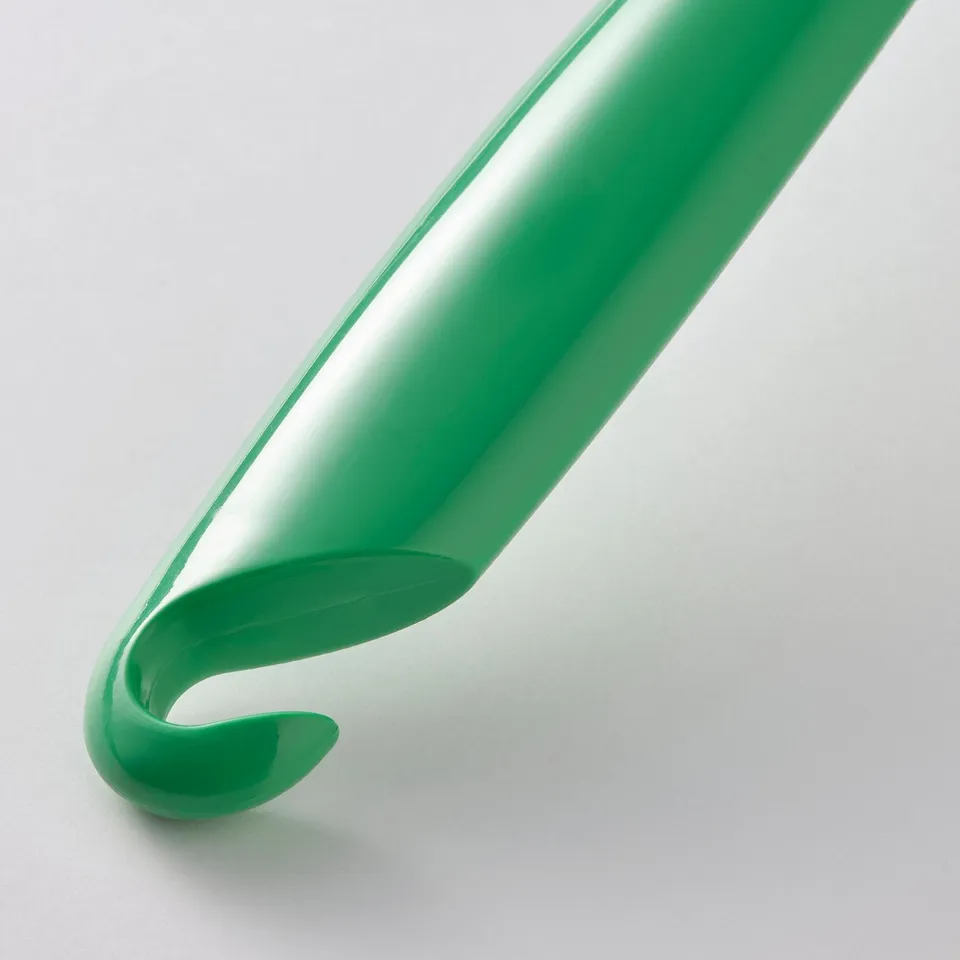 Green dishwashing brush with curved handle and bristles, designed for removing food debris, hangs for drying.