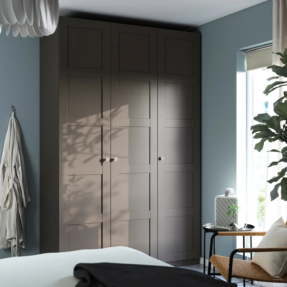 Minimalist bedroom with grey PAX wardrobe, blue wall, cosy bed, chair, plants.