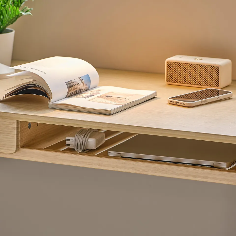 Wooden desk with built-in drawer and cable management, hosting books, phone, and speaker.