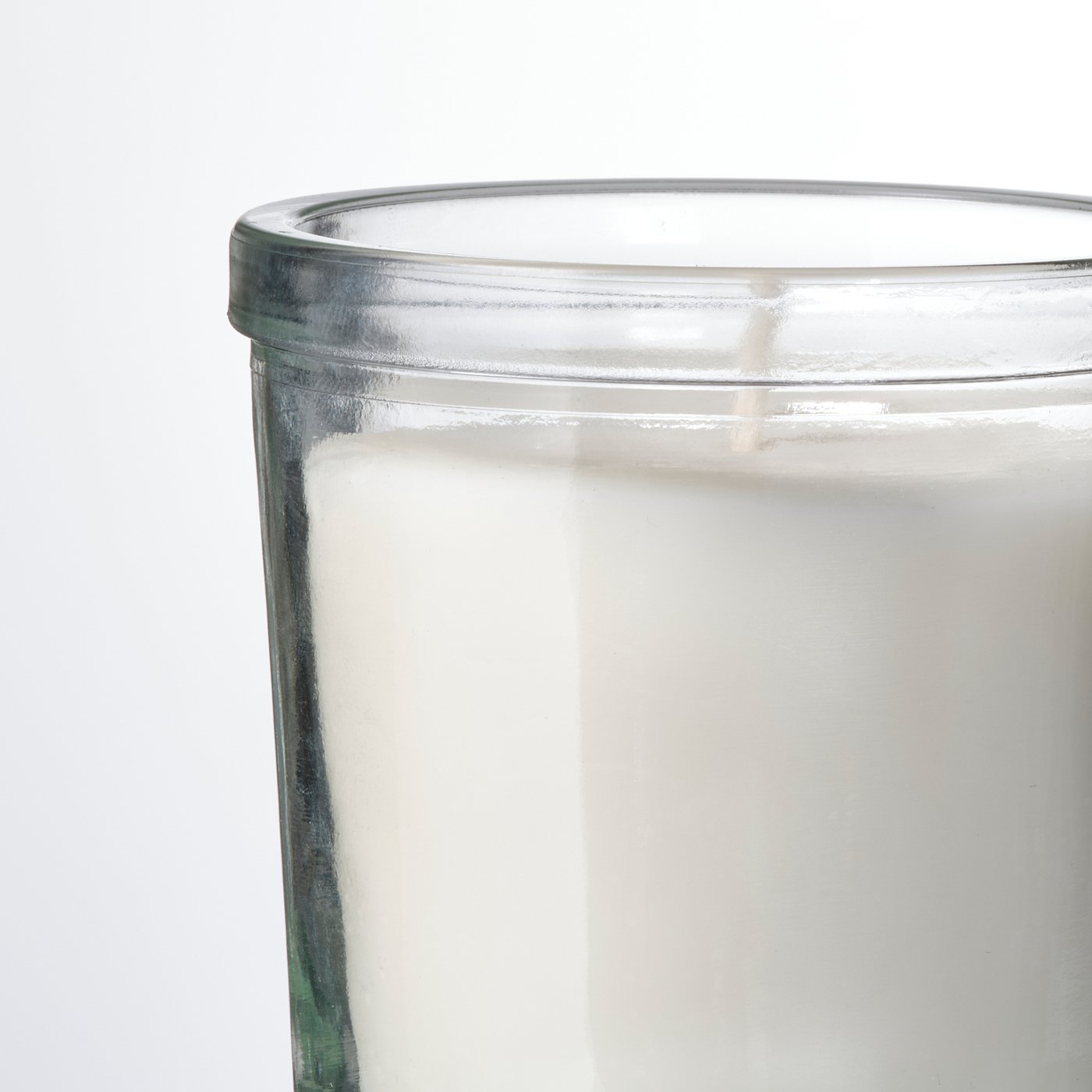 A transparent glass candle with a white label and visible white wax.