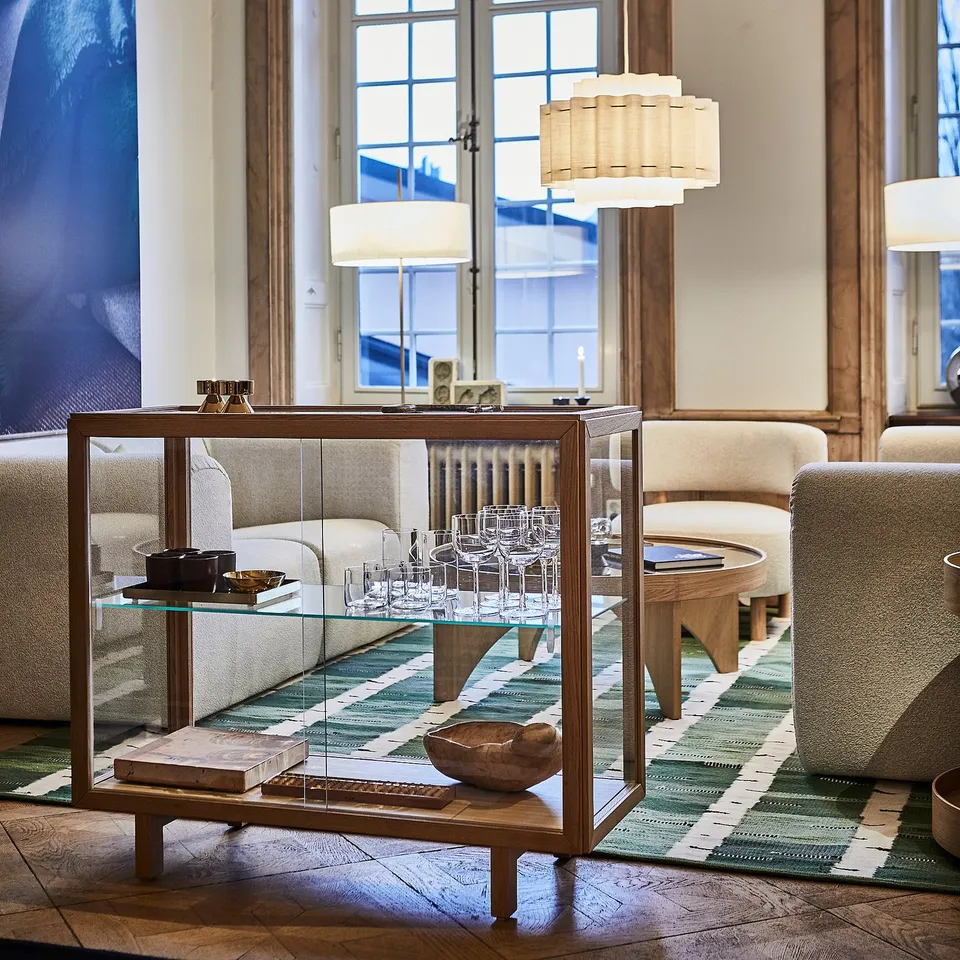STOCKHOLM 2025 glass cabinet in living room, displaying wine glasses & decor. Sleek, modern design with clear acrylic, oak, & tempered glass.