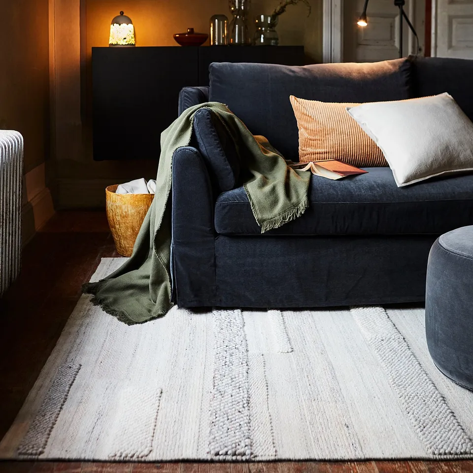 Living room with blue BRÖNDEN rug, sofa, candle, and pillows.
