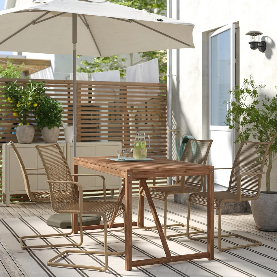 Outdoor dining set with wooden table and wicker chairs under a beige umbrella, perfect for relaxation.