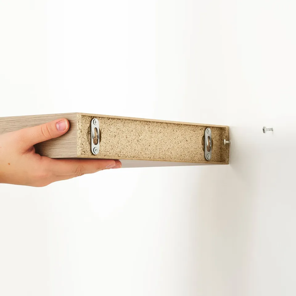 A hand holds a modern wall shelf, highlighting its sleek design and hidden suspension brackets. Ideal for saving floor space and displaying items.