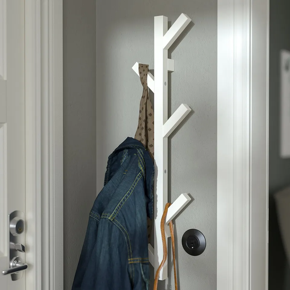 White wooden coat rack on wall holds jacket and hat.