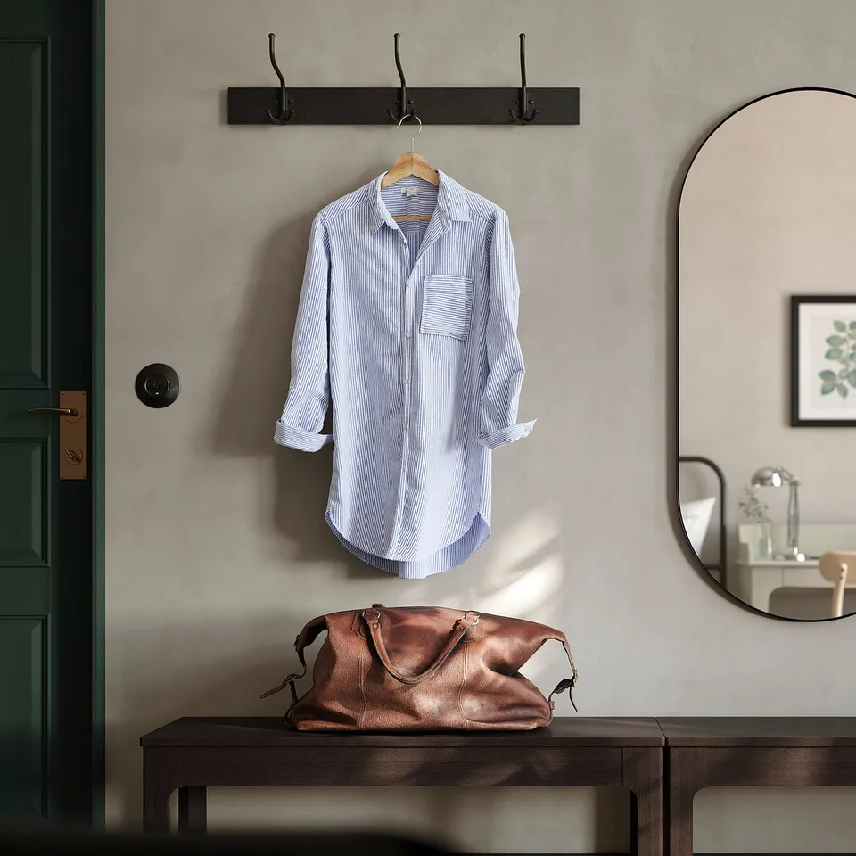 Grey entryway with blue-striped shirt on BUMERANG hanger, brown bag on dark bench, mirror reflecting decorated shelf.