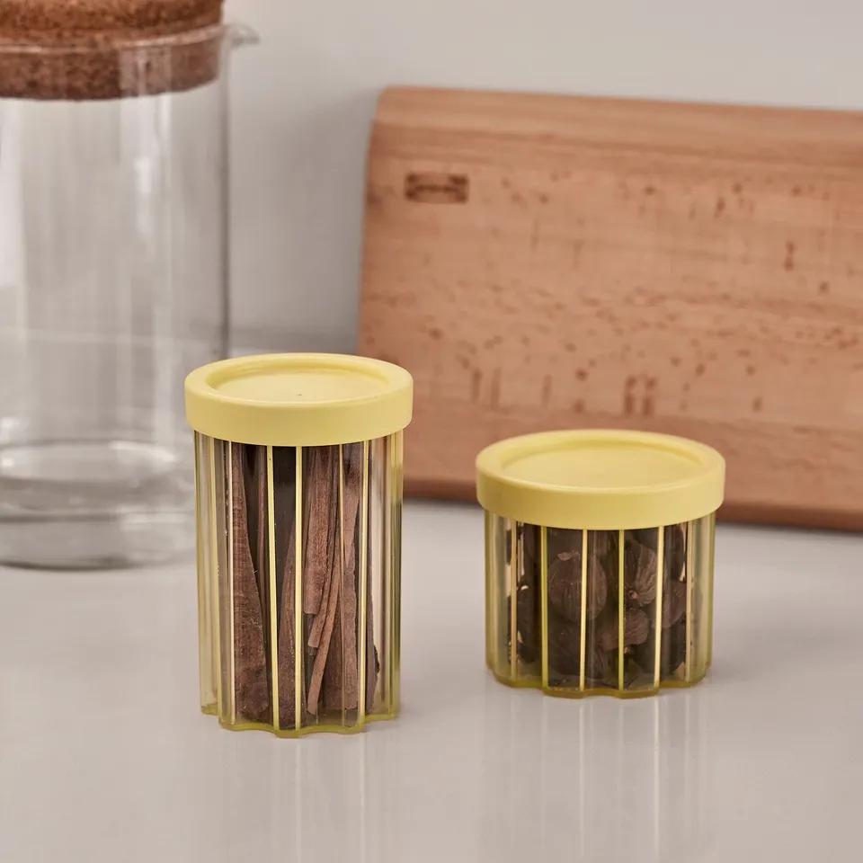 Small cylindrical jars with yellow lids and transparent bodies, holding herbs. Lightweight, stackable, and decorative for storage.