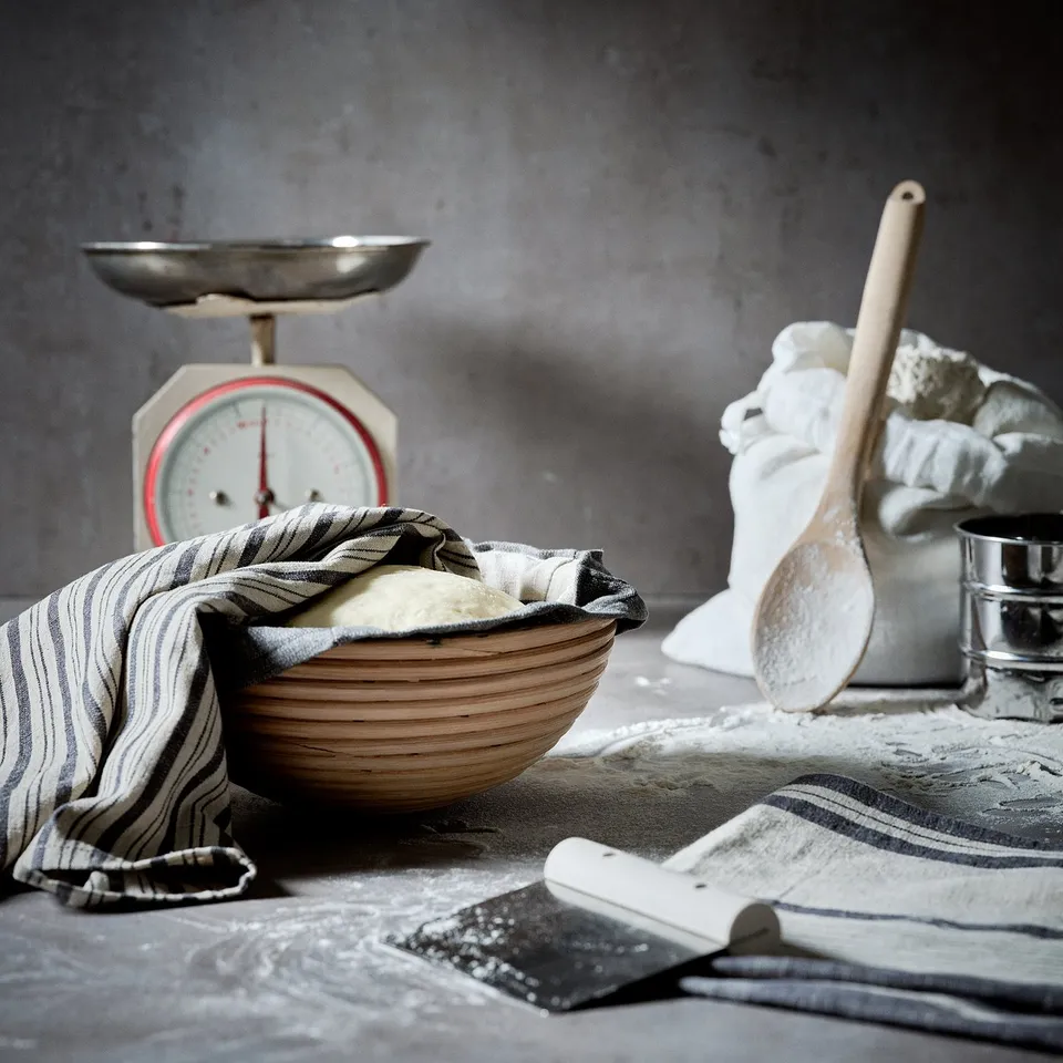 Old-fashioned scale, wooden dough bowl, flour cloth sack, utensils on flour dusted table.