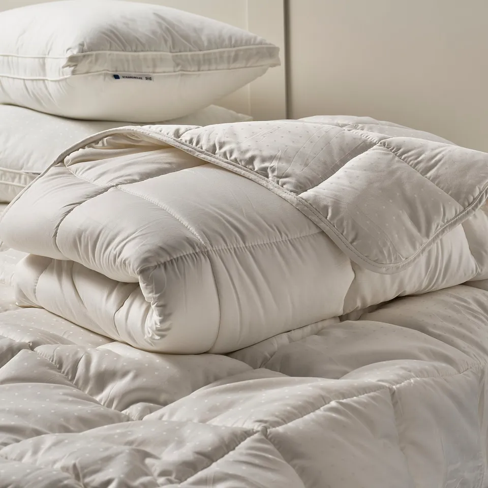 A white STRANDMOLKE duvet and pillows on a bed, quilted diamond pattern, inviting comfort.