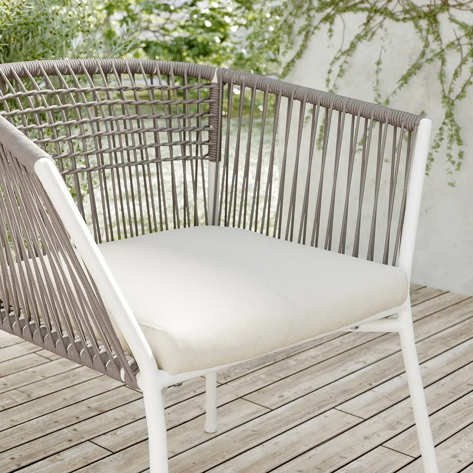 Modern white wicker patio chair with beige cushion on wooden deck.