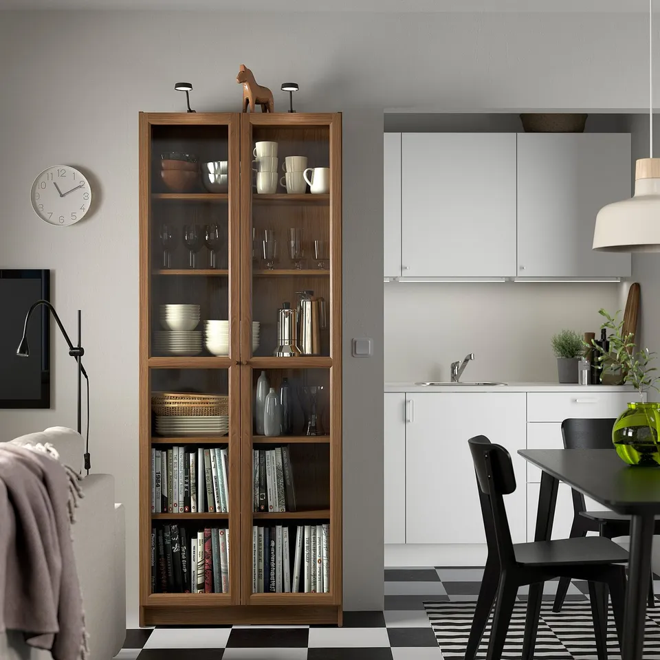 BILLY bookcase with glass doors next to kitchen, filled with books and decor.