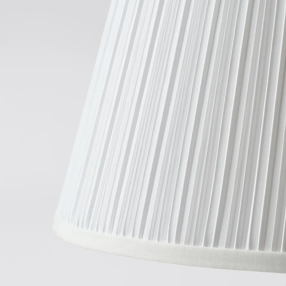 Close-up of white textured lamp shade. Fine vertical ribs create a delicate pattern, showcasing its quality.