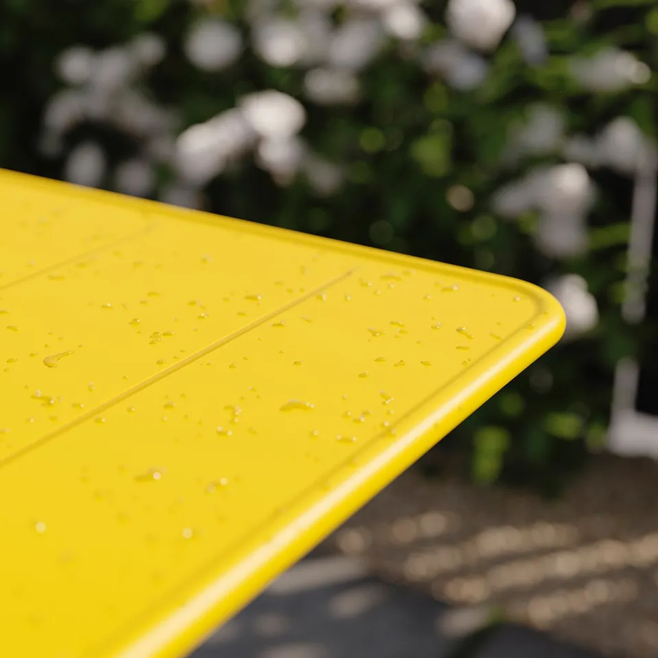 Bright yellow foldable outdoor table with rain droplets, surrounded by greenery.