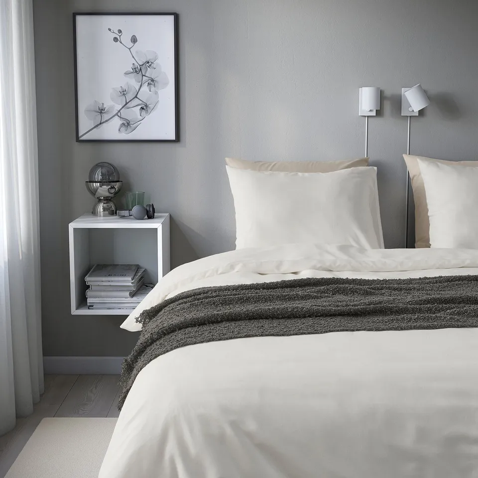 Minimalist bedroom with white PILTANDVINGE duvet, books, decor, and framed art.