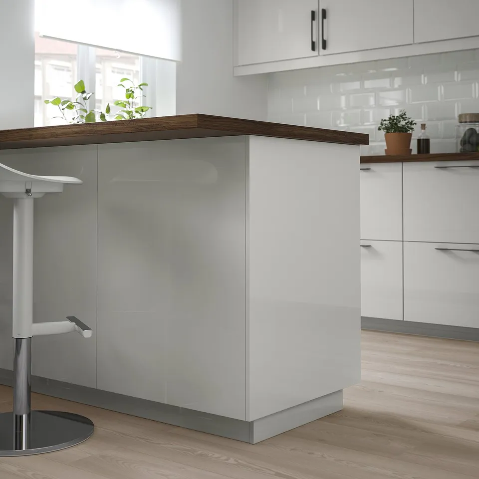 Modern kitchen with white glossy RINGHULT cabinets. Tall corner unit, sleek design, wooden floor, matching countertop.