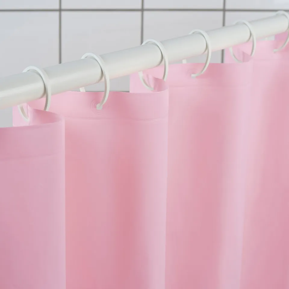 Light pink shower curtain hangs from white rod with rings, creating a harmonious and clean look in the bathroom.