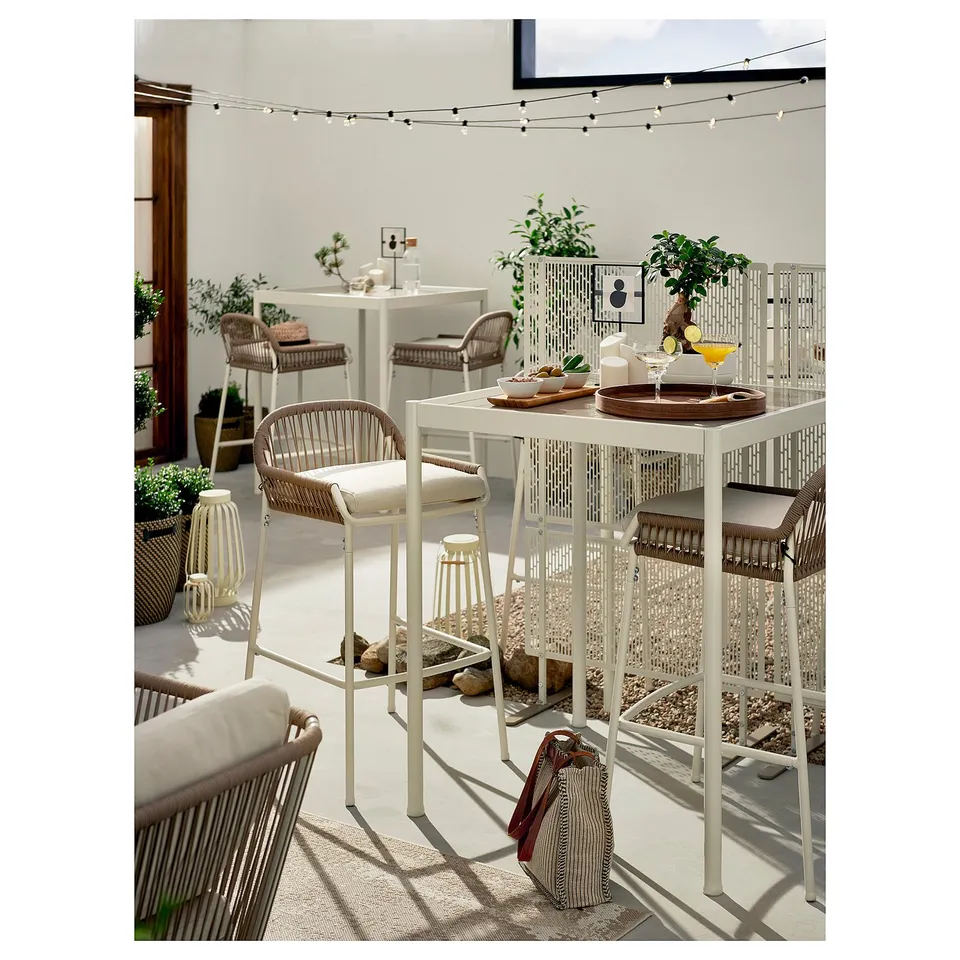 Modern outdoor dining area with white metal and wicker furniture, featuring LUNGÖN privacy screens, string lights, and potted plants.
