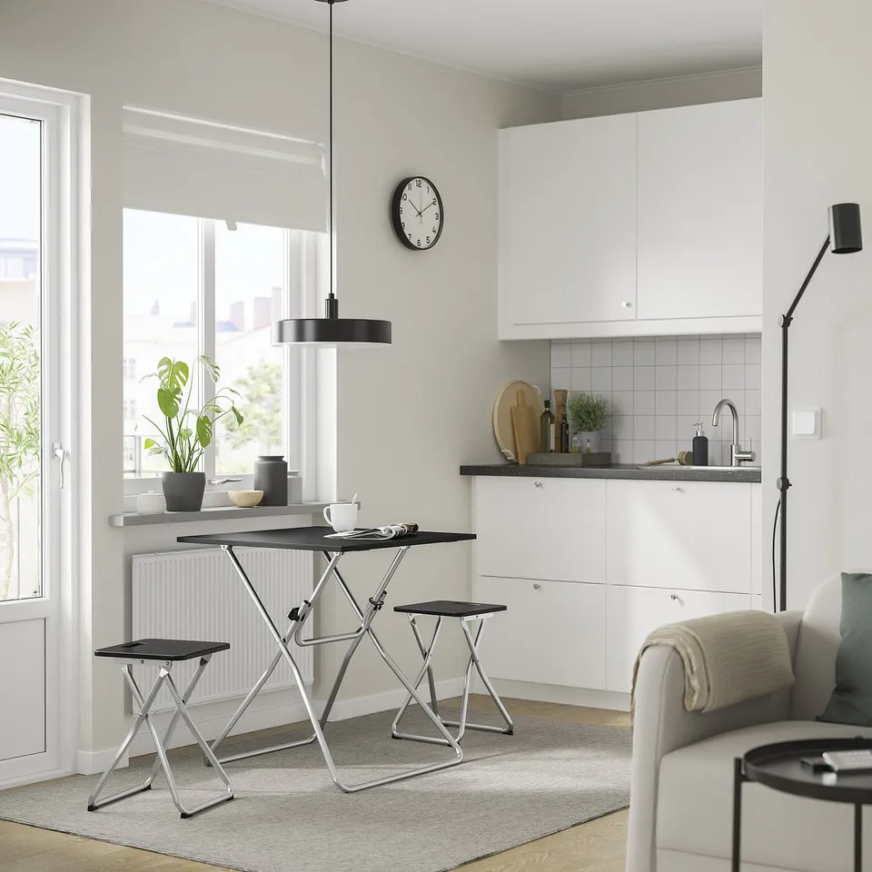 Modern kitchen with white cabinets, black metal table & stool, large window, compact for storage, stylish pendant light.