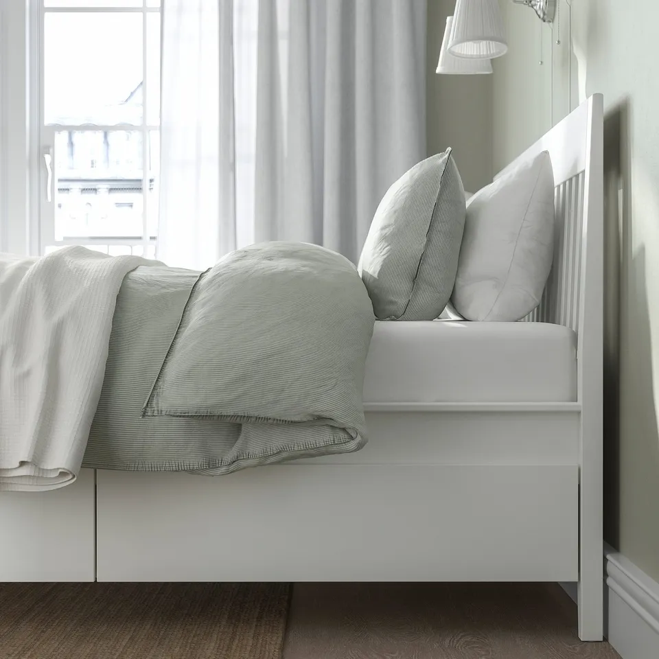 Bed with built-in drawers for extra storage, shown open with neatly folded bedding and pillows on a slatted base.
