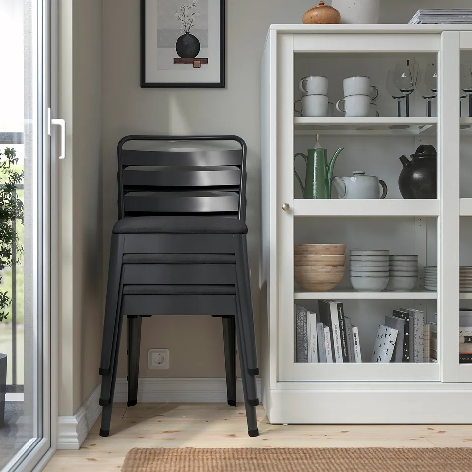Black metal SKOGSTA stool with wooden seat near kitchen shelf holding dishes and cups.