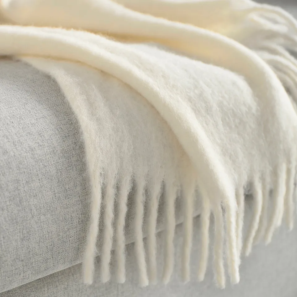 Fluffy, off-white throw blanket with fringes, draped softly, highlighting luxurious texture