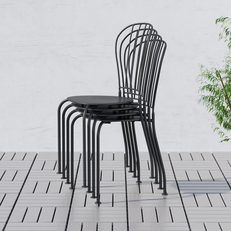 Black metal chairs stacked outdoors, back designed like wrought iron, seat circular with drainage hole.