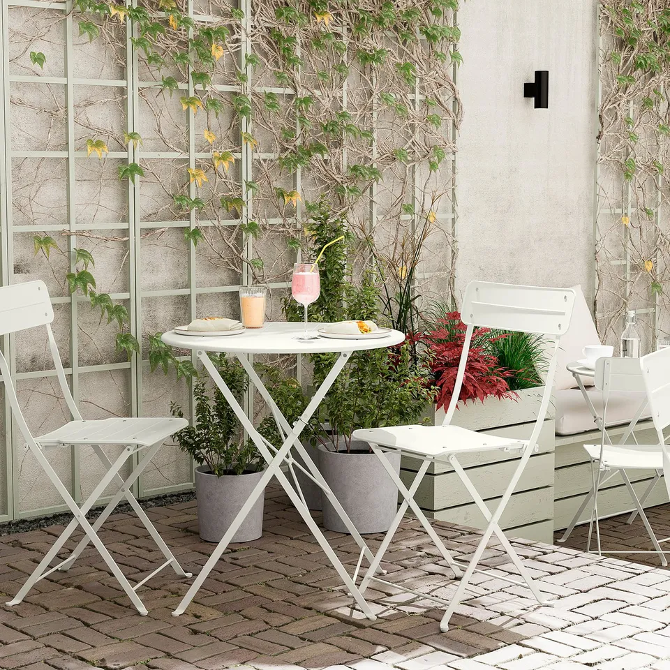 Small balcony setup with white metal table and chairs, potted plants.