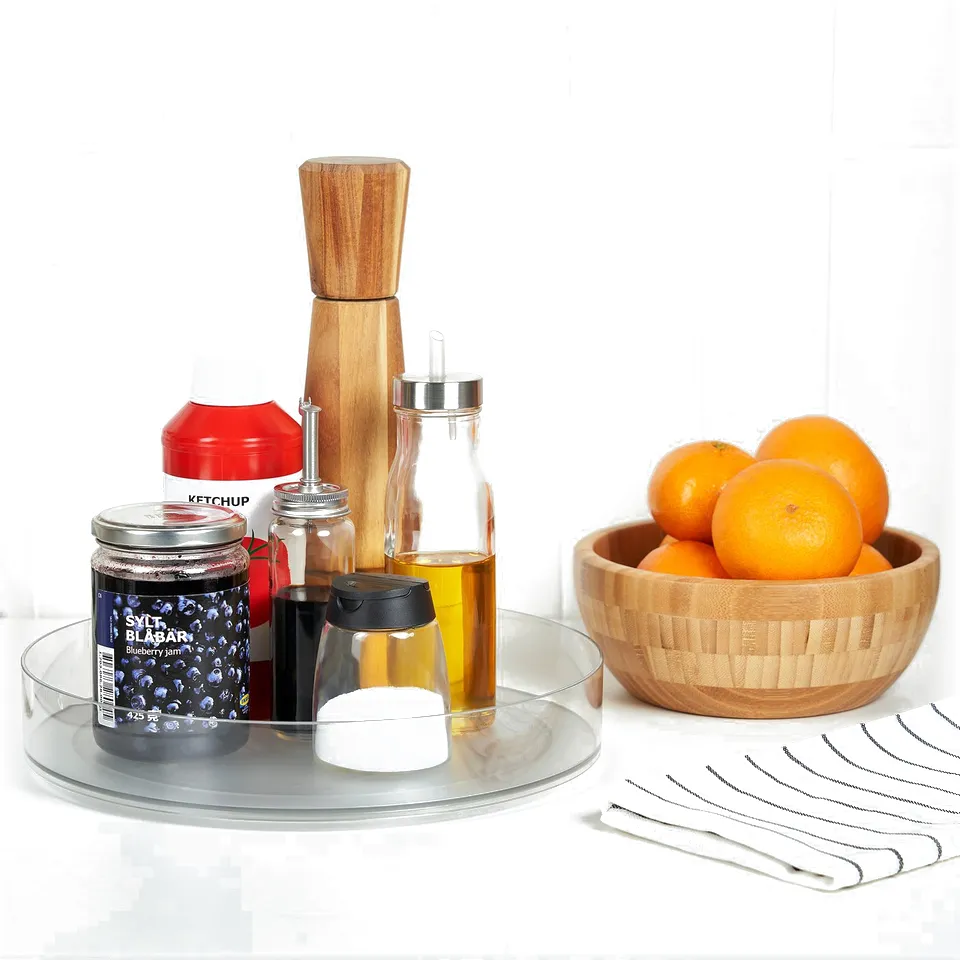Clear plastic turntable with fridge items: ketchup, jam, oil, oranges in wooden bowl, next to striped napkin.
