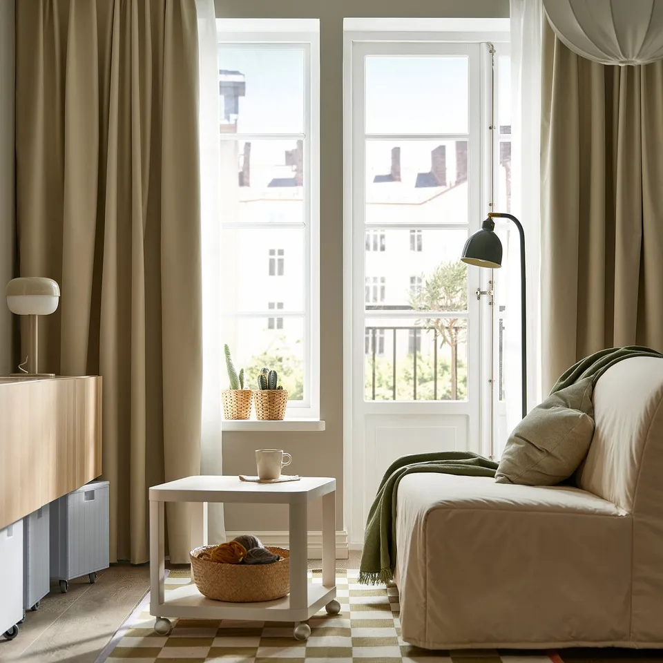 Modern living room with beige BENGTA curtains, a beige couch, small white table with coffee cup, and large windows letting in natural light.