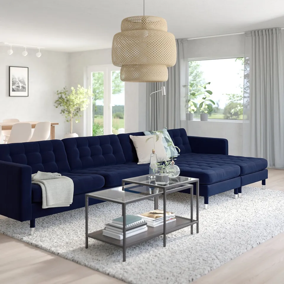 Modern living room with large navy blue l-shape sofa, glass-topped metal coffee table, and woven pendant light above.