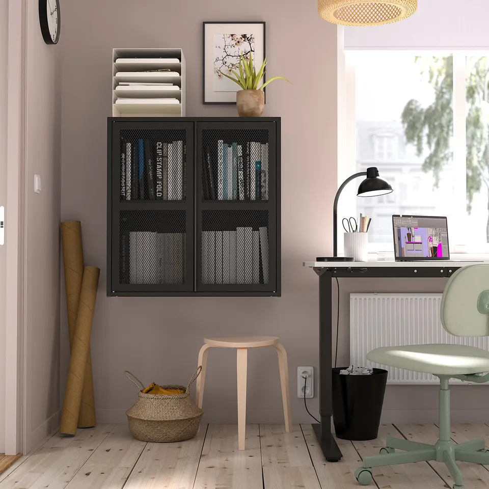Home office: black IVAR cabinet, files, books on pink wall. Wooden stool, desk with laptop, green chair.