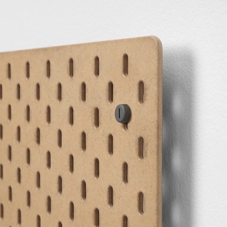 Pegboard with evenly spaced holes, light wooden texture, single dark round fixture fitted in hole.