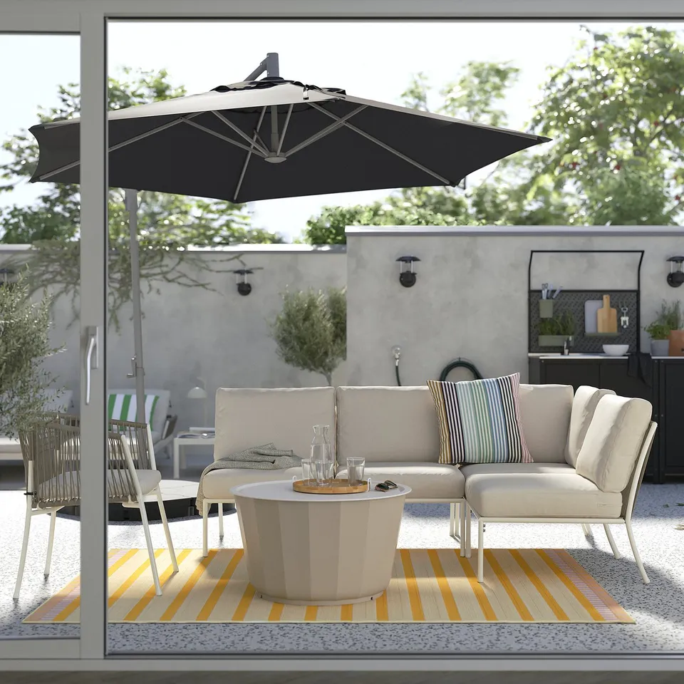Modern outdoor patio with white SEGERÖN lounge set, striped rug, black umbrella, and coffee table under a large window.