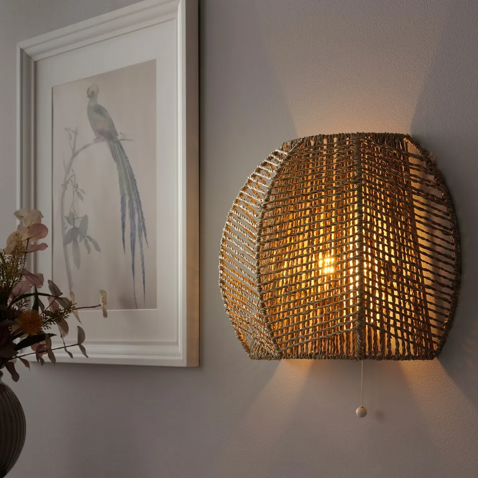 Woven wall lamp illuminates warmly, casting light in multiple directions.