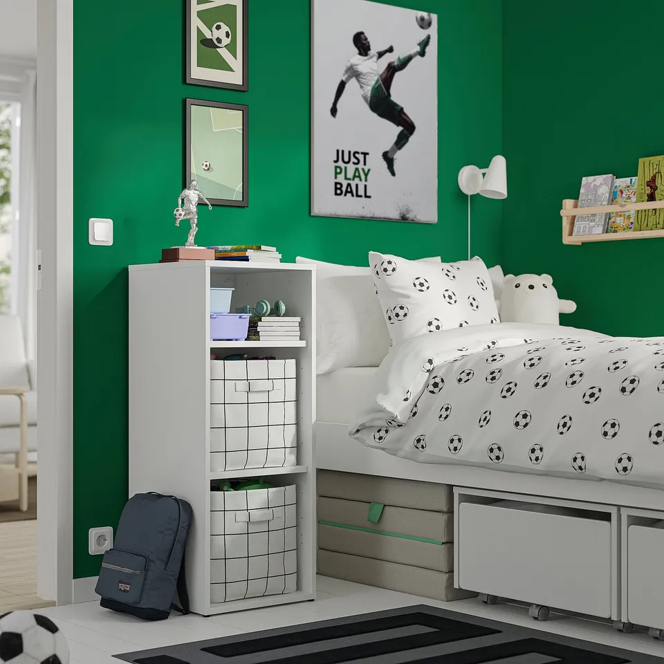 Kids soccer-themed room with green walls, white bed, storage unit, posters, and backpack.