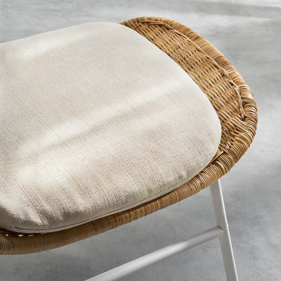 Modern footstool with beige cushion, woven wicker, sturdy legs.