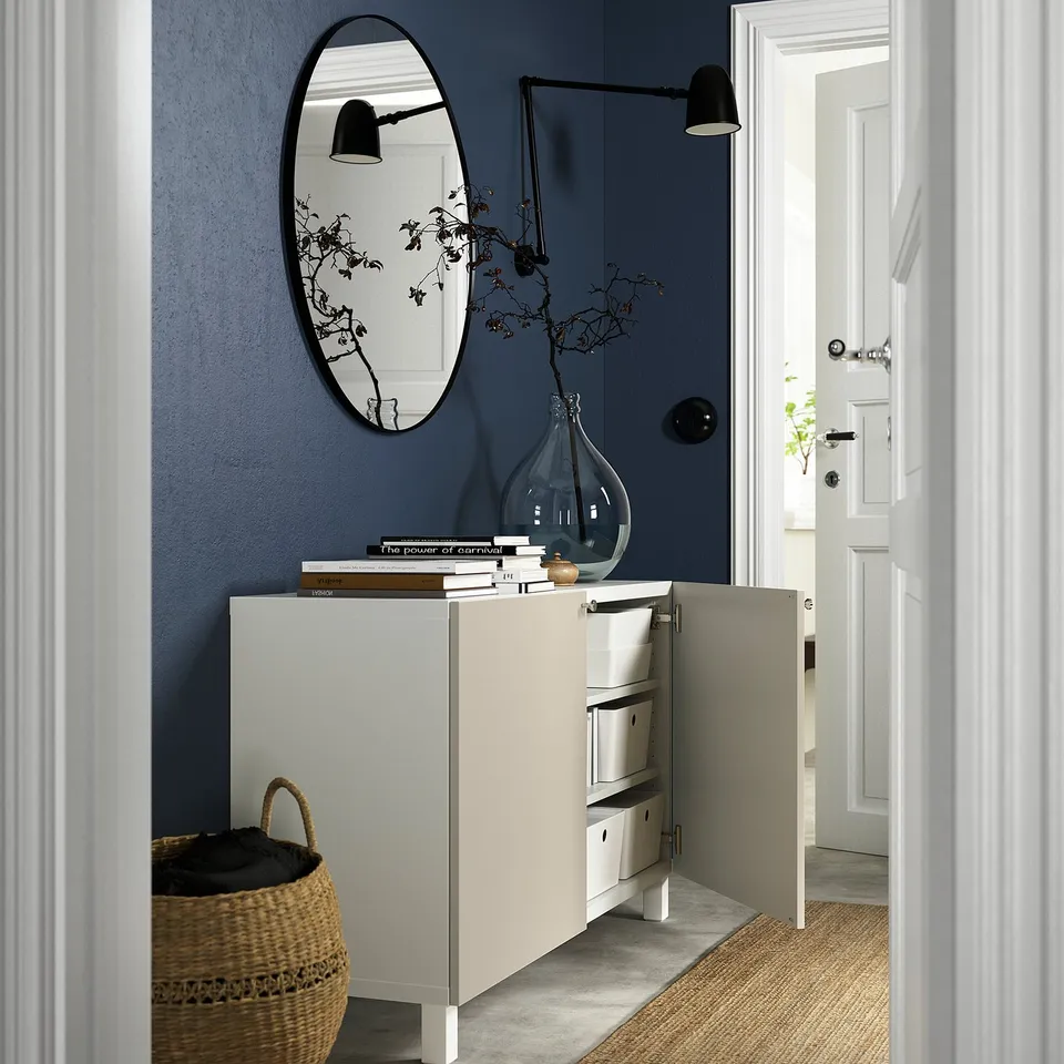 A hallway with a BESTÅ sideboard for storage and display, featuring a mirror, lamp, and decorative vase.