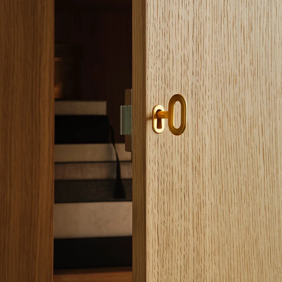 Golden door handle on light wood door opens to stairs, showcasing high-quality design.