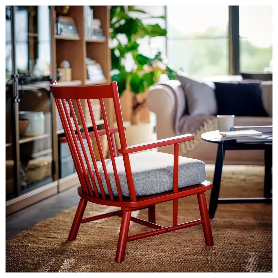 Red PERSBOL chair, wooden with spindle design, grey cushioned seat in cosy living room, near window and couch.
