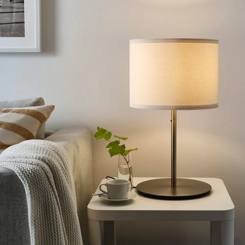 Small, modern lamp: RINGSTA. Gold base, white shade. On table by cosy couch.