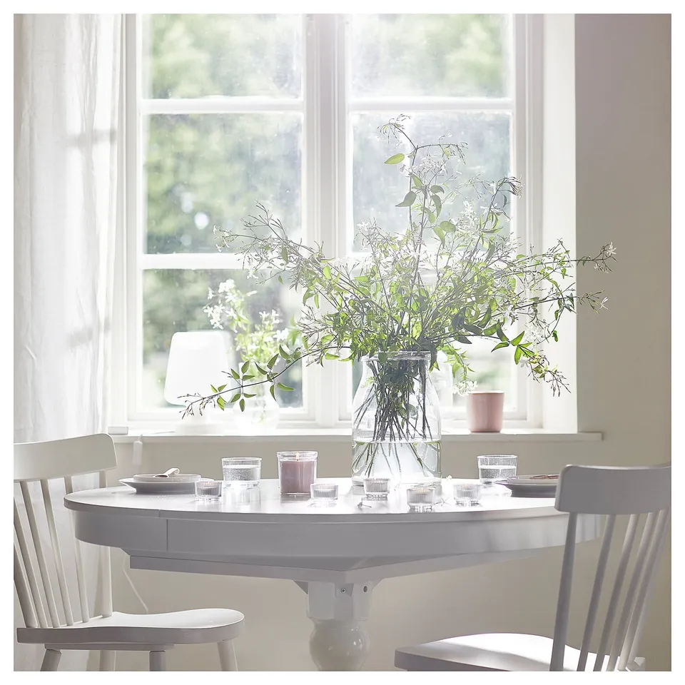 Bright dining area with round table, large window, and vase with lit candles.