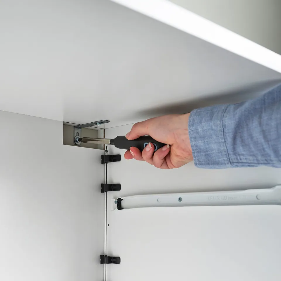 Person uses screwdriver to assemble minimalist storage chest, ensuring stability with wall anchors.