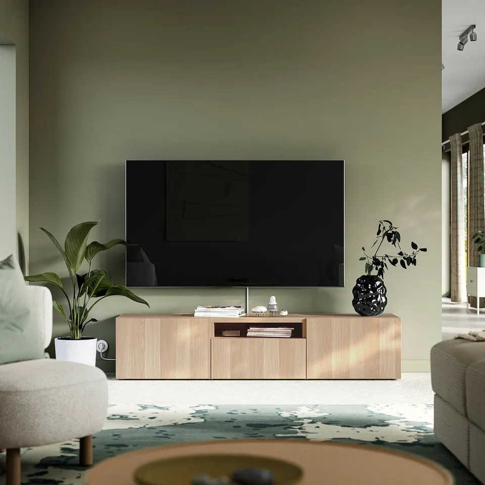 Modern living room with BESTÅ tv bench, green wall, flat screen tv, plants, sofa, and rug.
