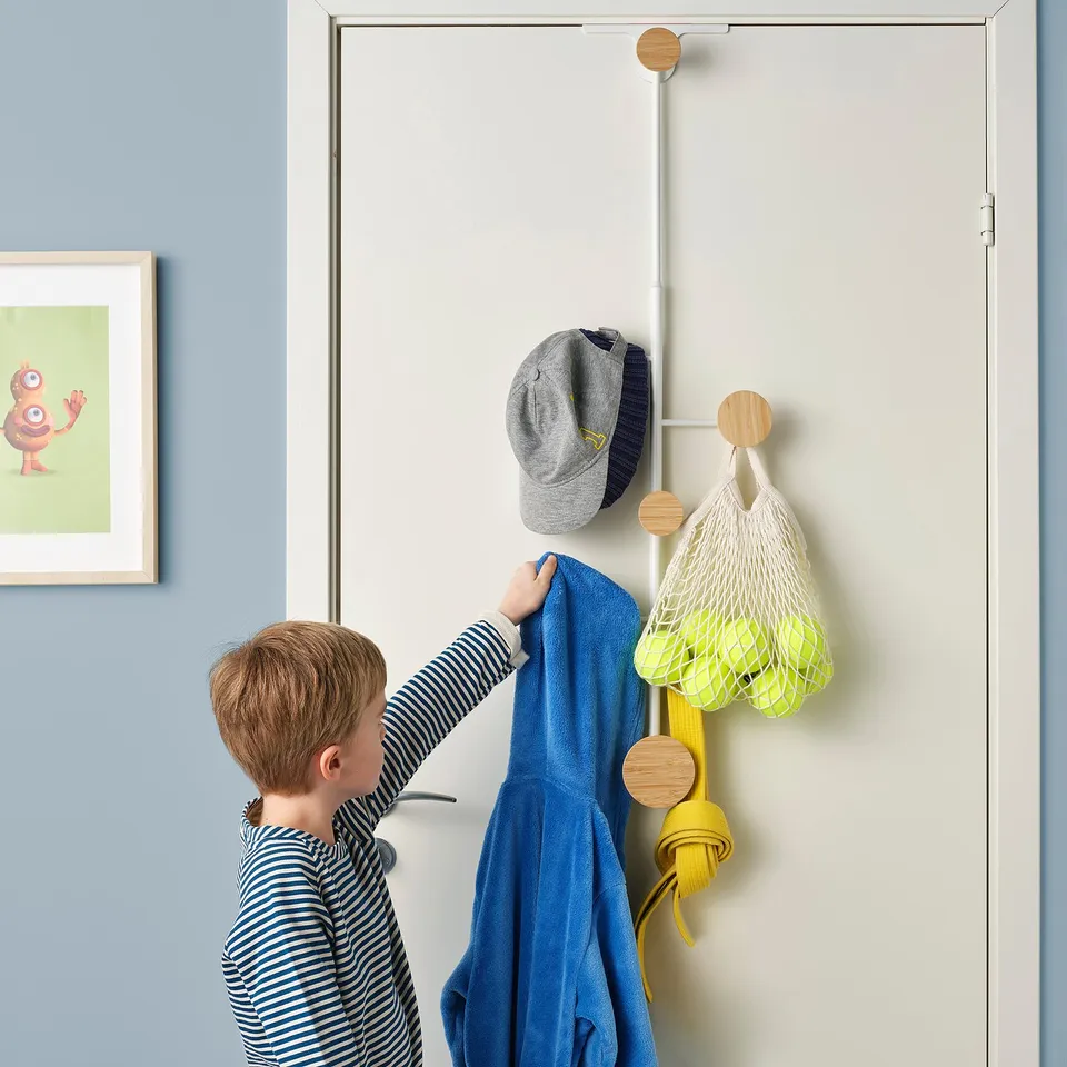 A kid hanging blue clothes on a BÄRFIS door hanger, demonstrating its adjustable height and storage function.