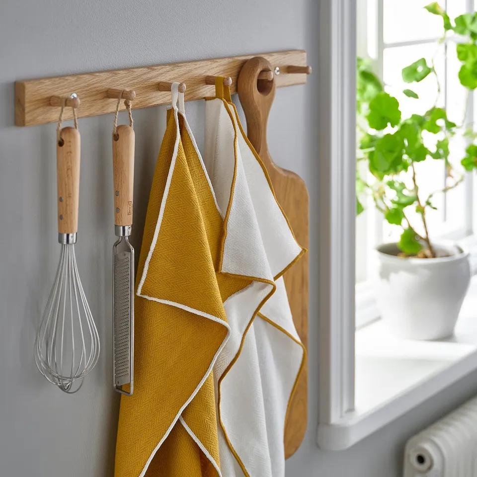 Kitchen hooks with utensils and towels. Whisk, grater, and chopping board hanging. Bright yellow and white towels with decorative edging.