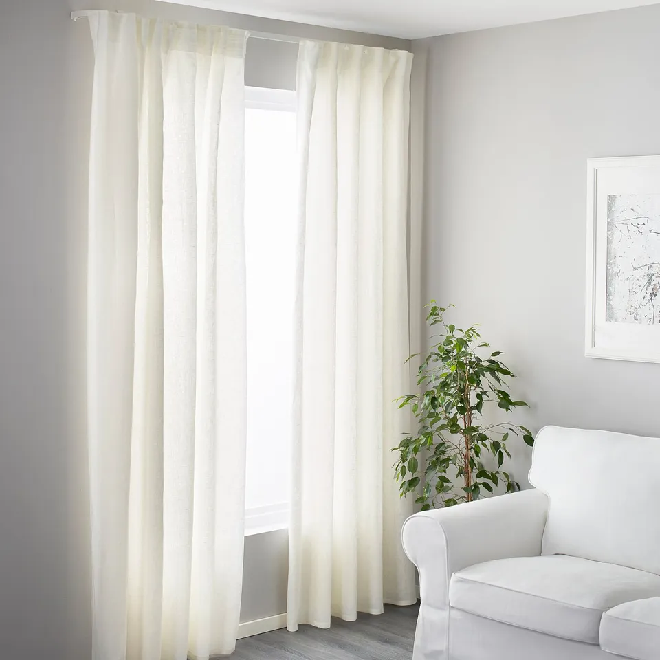 A minimalist room with white curtains framing a cosy couch and green plant.