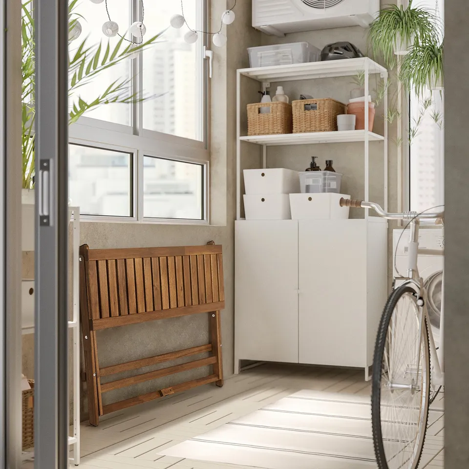 Foldable wooden bench NÄMMARÖ near white storage unit with bike. Bench is made of acacia, fits under window, smaller than bike.